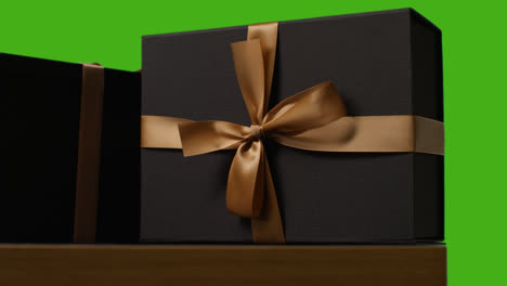 Close-Up-Of-Gift-Wrapped-Presents-Decorated-With-Ribbon-On-Table-Shot-Against-Green-Screen